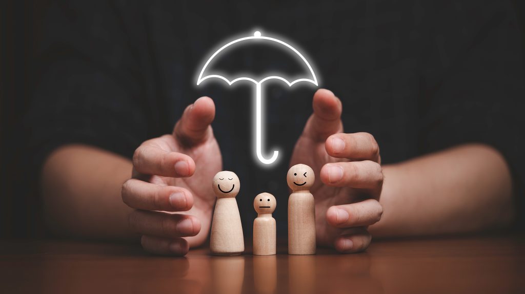Wooden peg dolls with smiling faces protected by a glowing umbrella held by hands above them, symbolizing protection.